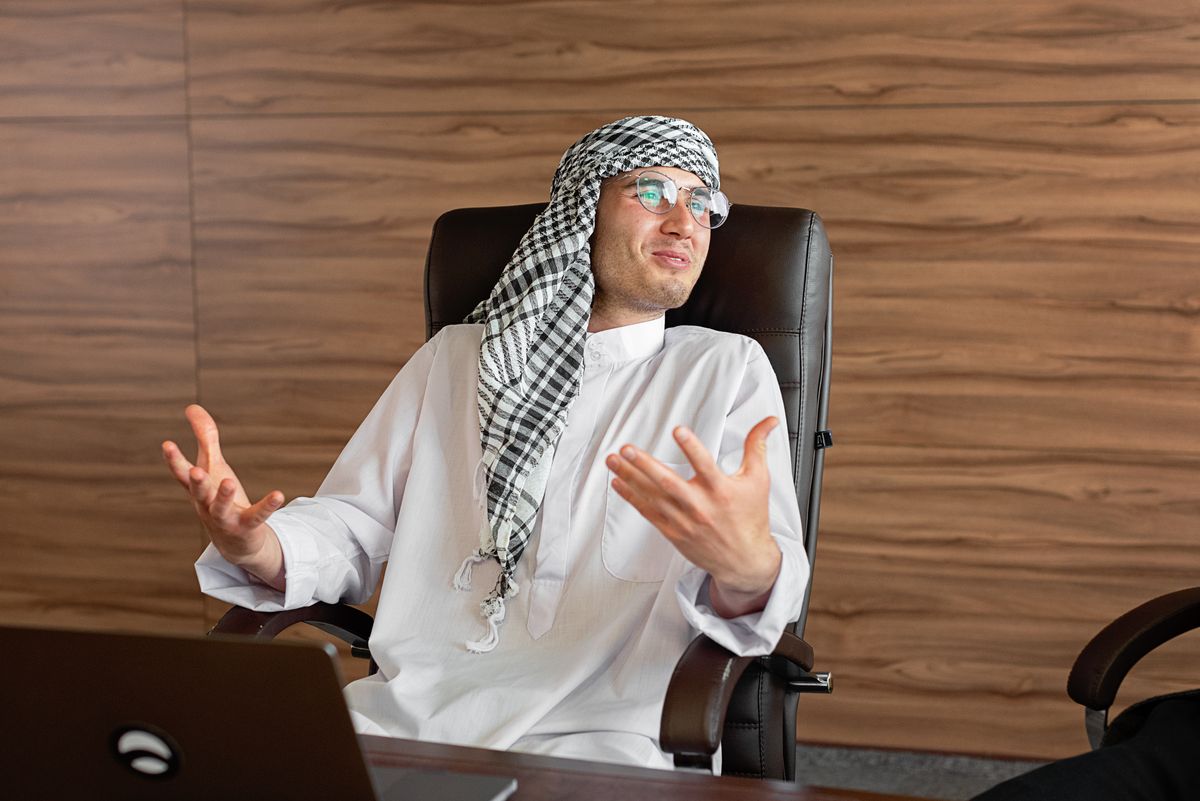 An Arab professional in traditional white attire discussing business in an office