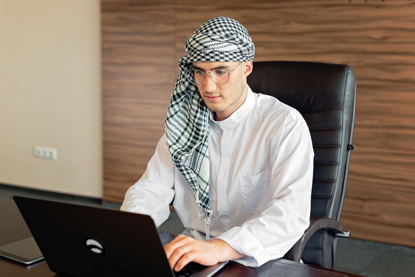 An Arab professional in traditional attire working on a laptop